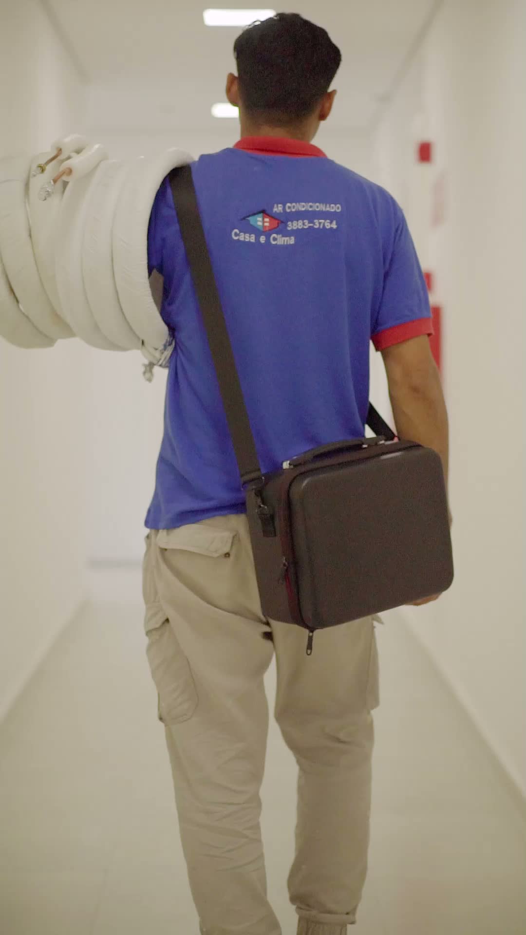 Técnico da Casa e Clima caminhando com tubulação isolada e maleta de ferramentas